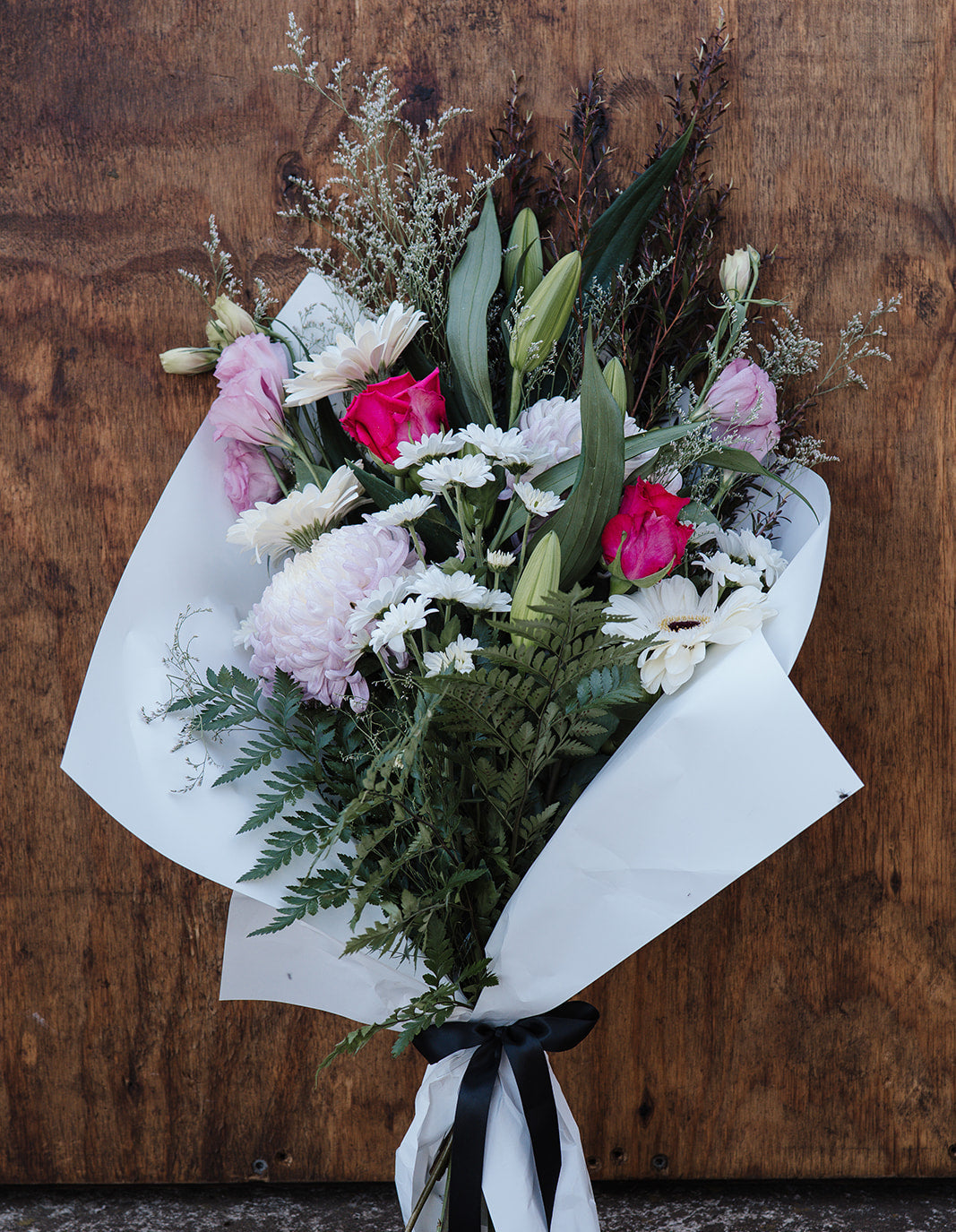 Bouquet of flowers wrapped in white paper with a black ribbon against a wooden background